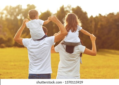 View From Behind. A Family With Children Are Walking On The Grass In A Park .