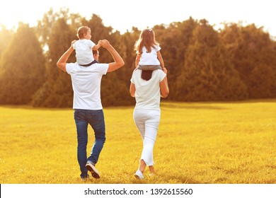 View From Behind. A Family With Children Are Walking On The Grass In A Park .