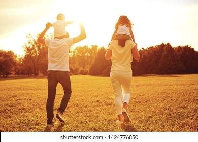 View From Behind. A Family With Children Are Walking On The Grass In A Park .