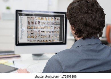 View from behind over his shoulder of a photographer editing photos on a computer with rows of images visible on the monitor - Powered by Shutterstock