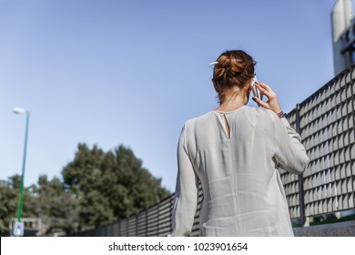 View From Behind Of A Slim Woman Talking To Her Mobile Phone, On A Sunny Day