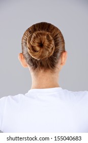 View From Behind A Woman With Her Brunette Hair Done In A Neat Bun On The Back Of Her Head Against A Grey Studio Background