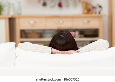 View From Behind Of A Young Woman Relaxing At Home On A Couch With Just The Top Of Her Head And Her Arms Visible Above The Cushions