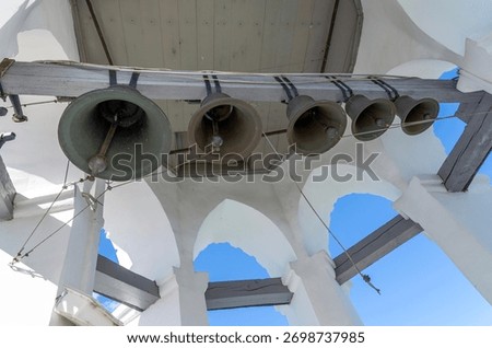 View of the bells from bottom to top. The interior of the bell tower. A row of bells of different sizes suspended from a wooden beam. 
