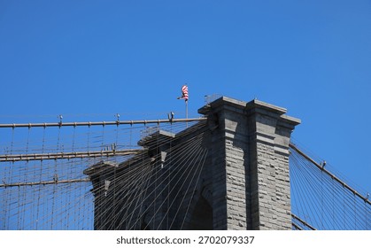 view from below the brooklyn bridge structure and the american flag flying above the cables