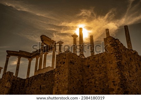 View from below of the capitals, cornice and columns of the Roman theater in Mérida, with the sun backlighting at sunset creating a divine flash of a spectacular cloudy sky.