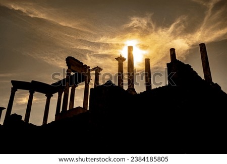 View from below of the capitals, cornice and columns of the Roman theater of Mérida, with the sun backlit at sunset creating a divine flash of a spectacular sky with clouds as rays of light.