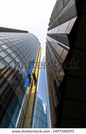 View from below of a cleaning worker on a scaffold or hanging gondola to clean the glass facade of a glass skyscraper in the City of London with his reflection in the facade.