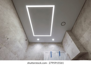 A view from below of the integrated, concealed access hatch in the white suspended ceiling. When closed, the hatch with a perimeter LED profile functions as modern built-in lighting in the bathroom.
