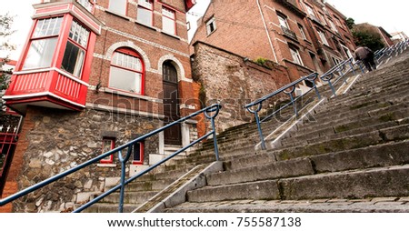 View from below of a man climbing a stairway of concrete, with a blue rail, within a urban context, surrounded by red bricks houses. - Liegi, Belgium