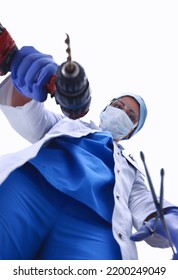 View From Below Of Masked Doctor Scaring The Patient With A Drill .