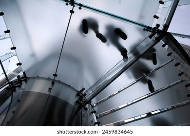View from below of people walking down clear spiral stairs