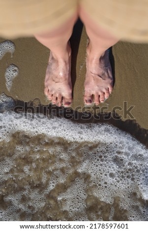 View below to woman barefoot legs from her head standing on sand in wave of Baltic sea