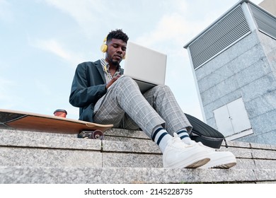 View from below of a young African-American adult man on a skateboard while working on a laptop computer - Powered by Shutterstock