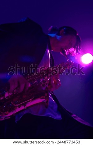View from below of young talented man playing sax in vibrant pink neon light against dark studio background. Concept of music and art, hobby, concerts and festivals, modern culture. Ad