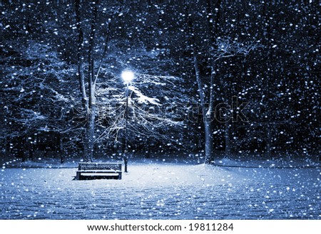 View of bench and shining lantern through snowing. Night shot.
