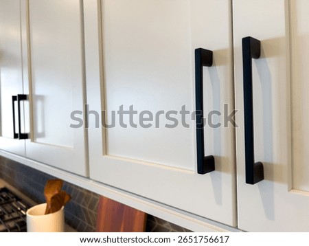 View of black vertical pulls on white kitchen drawers below a wooden countertop. Neutral kitchen design with modern accents.