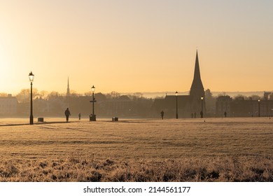 A View Of Blackheath Common In The Winter During A Warm Sunset. All Saints Church Can Be Seen In The Distance And People Can Be Seen Walking.