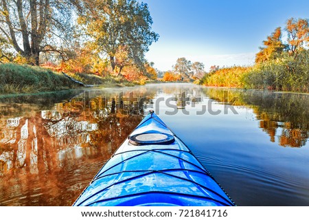 View from the blue kayak on the river banks with autumnal yellow leaves trees in fall season. The Seversky Donets river, autumn kayaking. Selective focus at nose kayak's part.