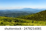 A view of the Blue Ridge mountains from the Appalachian Trail atop Round Bald in Tennessee-North Carolina. Layers of grasslands, forests, and distant mountain peaks.