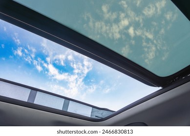 View of a blue sky and clouds through an open car sunroof, emphasizing freedom and travel.