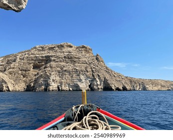 View from a boat approaching rugged limestone cliffs over deep blue water under a clear sky. A scenic coastal adventure showcasing natural rock formations and vibrant ocean colors. - Powered by Shutterstock