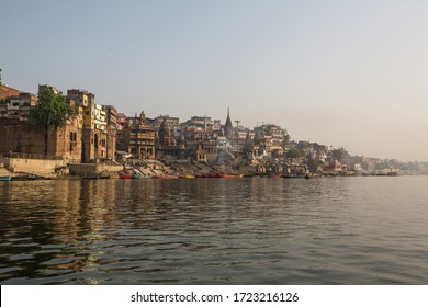 View from a boat glides through water on Ganges river along shore of Varanasi, India.