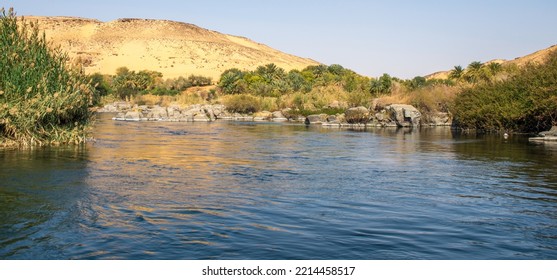 A View From The Boat Looking At The West Bank Of Nile River In Egypt Showing The Running Water Coming From Africa And The Desert Mountains With Sands Along With Green Palm Trees