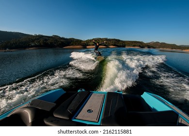 View From Boat On Athletic Man In A Black Wetsuit Masterfully Jumping With Wakesurf Board On A Wave