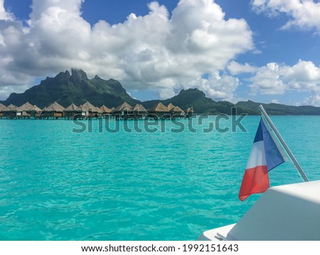 View of Bora Bora Island and bungalows from the water. Taken from a boat. French flag in the foreground. Tahiit, French Polynesia.