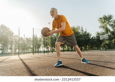 View from the bottom. Caucasian handsome motivated strong senior male athlete playing basketball at outdoors summer court. People. Competitive sports games. Active healthy lifestyle in retirement - Powered by Shutterstock