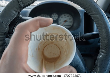 view of the bottom of an empty Cup of cocoa drunk in the driver hand on the background of the steering wheel and dashboard of the car