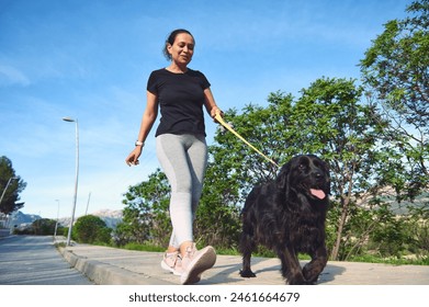 View from the bottom of a multi ethnic happy young woman in sports clothes, walking her dog on leash and enjoying morning run with her pet in the mountains nature. People and playing pets concept - Powered by Shutterstock