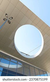View from the bottom of a round element of modern office building's design against blue sky background. Upgrowing perspective.
