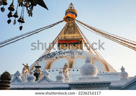 View of the Boudhanath Stupa in Kathmandu Nepal against a blue sky in warm evening light. There are many pigeons on the roof. In the foreground blurred bells.