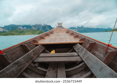 A view from the bow of a wooden boat on a serene lake, surrounded by mountains and cloudy skies. - Powered by Shutterstock