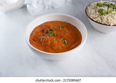 A view of a bowl of butter chicken, with a bowl of basmati rice.