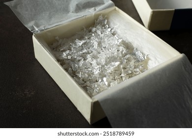 A view of a box full of silver leaf sheet pieces.