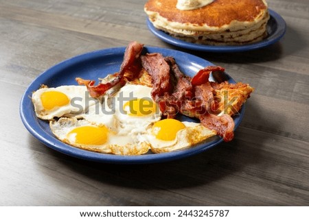 A view of a breakfast combo, featuring fried eggs, bacon, hash browns, and pancakes.