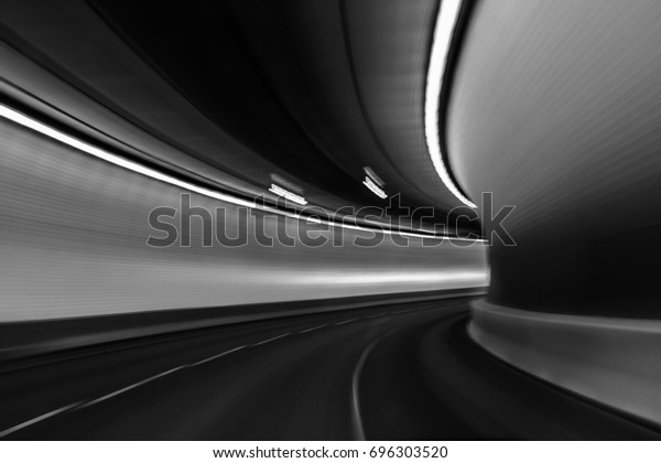 View of the\
brightly lit tunnel from a fast moving car; light blur exaggerates\
the movement; black and\
white