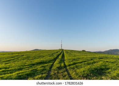View of a broadcasting tower lying on a hill in the middle of a landscape in a field on a hill.