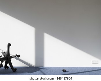 View Of A Broken Office Chair Casting Shadow On Wall