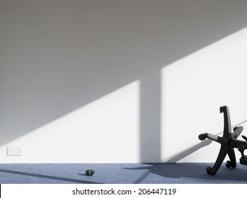 View Of A Broken Office Chair Casting Shadow On Wall