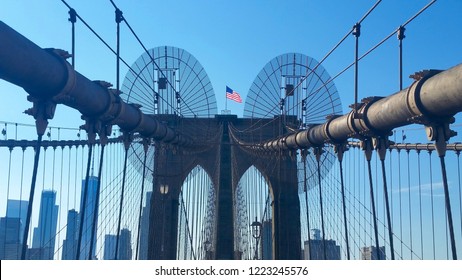 View of Brooklyn Bridge from footpath with pedestrian safety netting and barrier with centralized American Flag aloft bridge tower overlooking Manhattan Skyline - Powered by Shutterstock