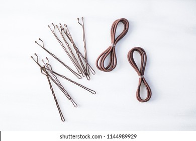 View of brown bobby pins, brown hair bands against a simple white background