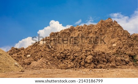 View of brown mounds dug up and dumped on the ground waiting to prepare for the landfill to improve construction with clouds in the sky in the background.