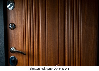 View Of A Brown Steel Metal Door With Wood Trim. Multiple Locks And A Handle