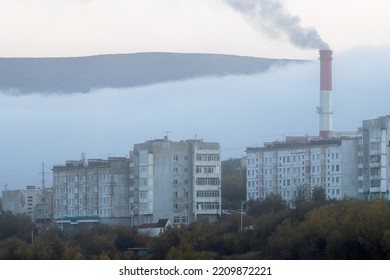 View Of The Buildings Of A Residential City Block And A Smoking Chimney Of A Coal-fired Combined Heat And Power Plant. Foggy Weather. Ecology In The Cities Of Siberia. Magadan, Magadan Region, Russia.