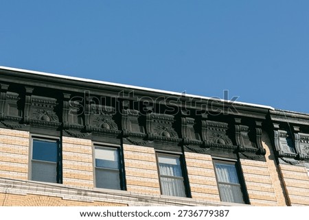 A view of a building's upper section showing detailed design along the cornice while the sun shines in the sky.