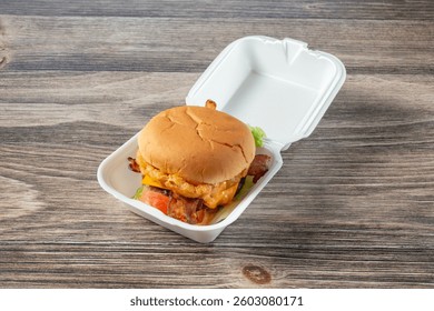 A view of a burger in a clamshell styrofoam container.